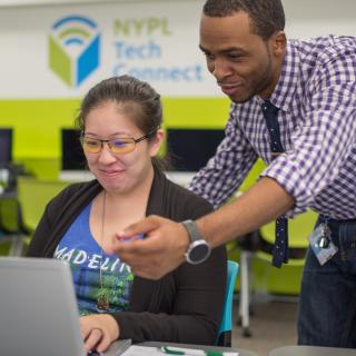 A man assisting a woman at a laptop computer