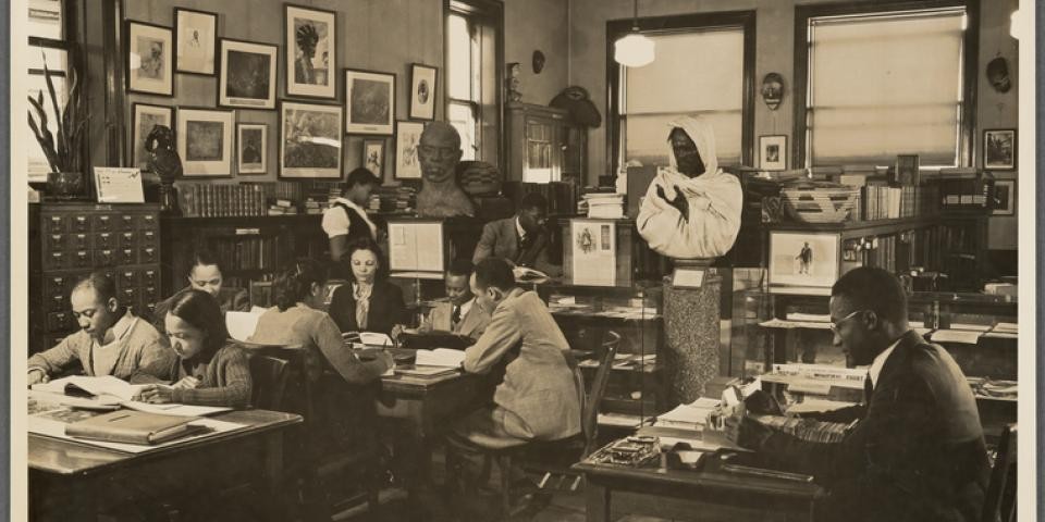 Reading room of the Schomburg Collection at the 135th Street Branch Library, circa 1938 - 1945, tables full of Black men and women viewing library collections. Lawrence Reddick, curator, seated at right.