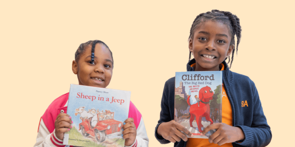 Two young girls holding up books and smiling.