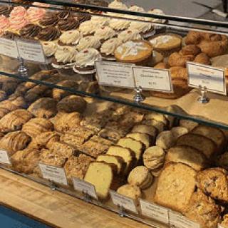 Photo of a glass bakery case filled with bread and pastries along with small signs in front of each series of items