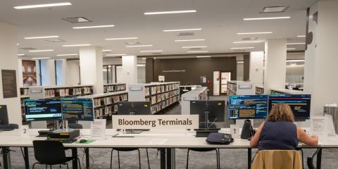 Interior photo of the Thomas Yoseloff Business Center featuring a long table with Bloomberg Terminals and a person studying data at one of the terminals in the foreground. 